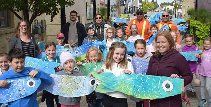 A group of people holding up fish sculptures in Port Hope